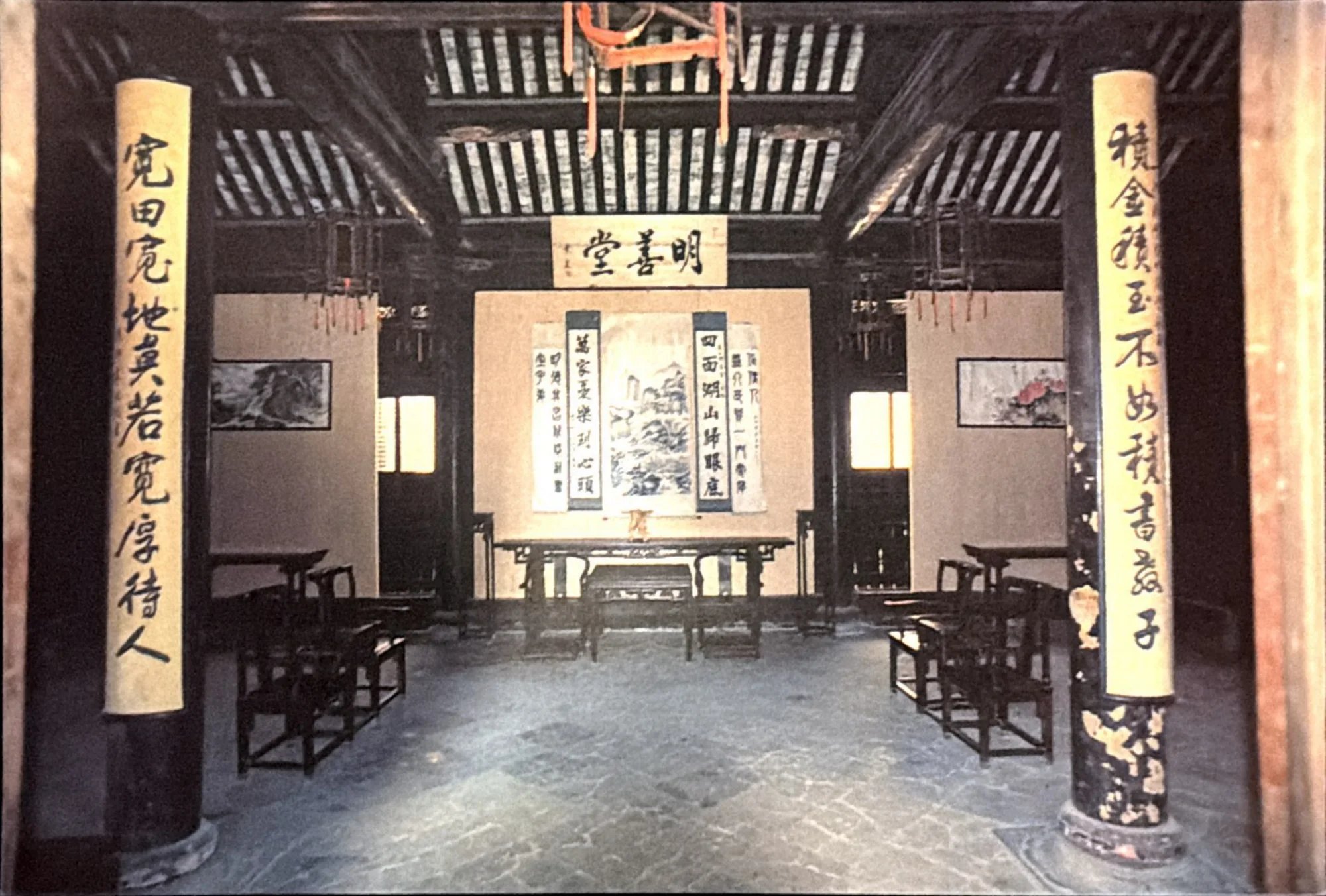 Photograph of a traditional Chinese hall with dark wooden columns carrying vertical calligraphy and a central scroll painting.