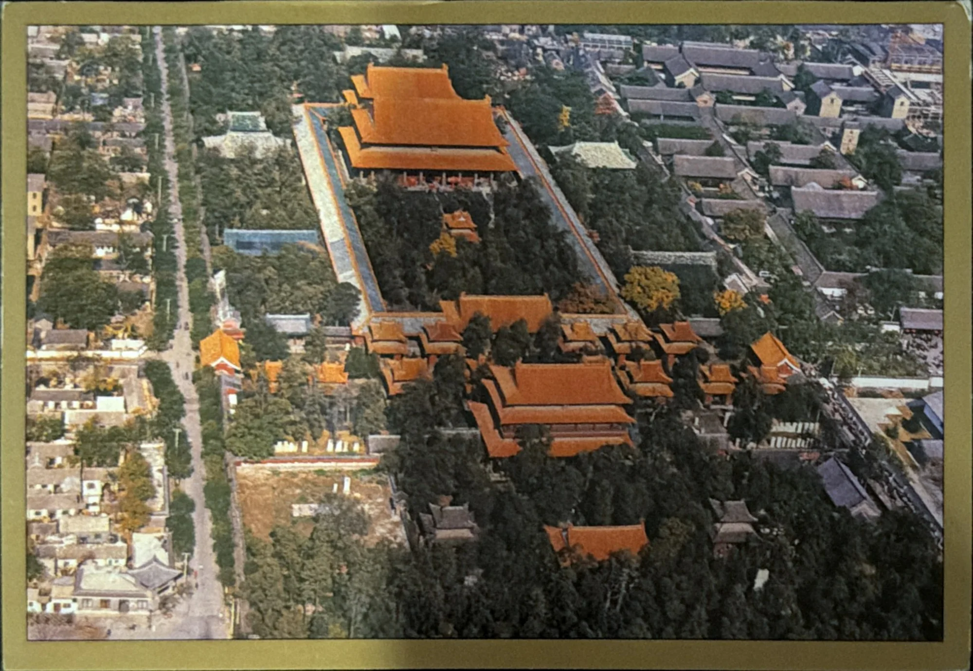 Aerial photograph of a long walled compound of orange-roofed halls surrounded by low grey city blocks.